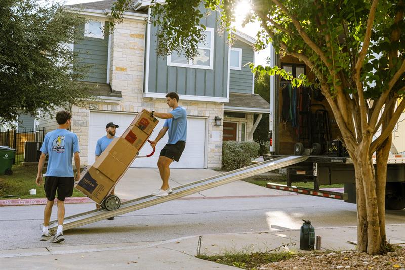 Three Butter Brothers movers rolling a stack of boxes up the truck ramp